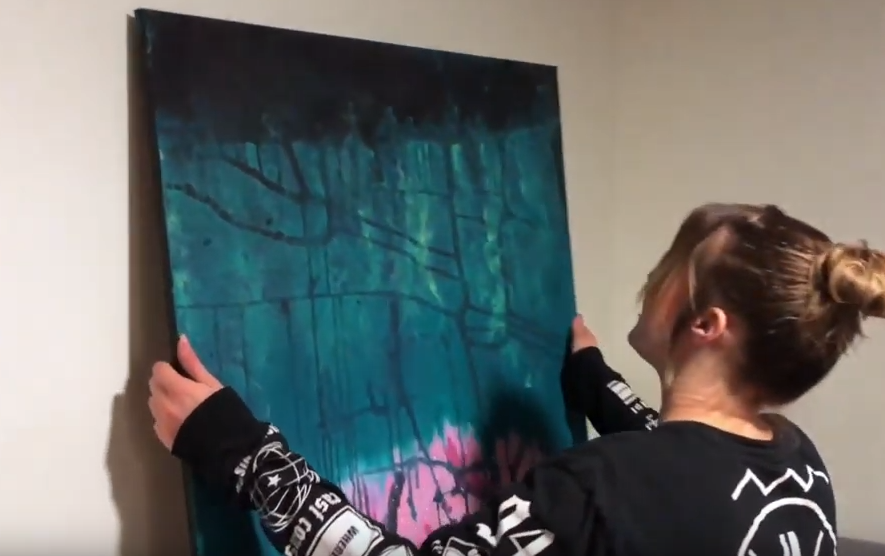 Jennifer sätter upp ett konstverk på väggen