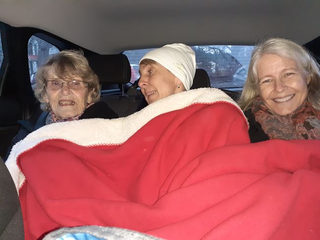 Tre äldre damer sitter i baksätet på en bil. De har en skön filt i knät