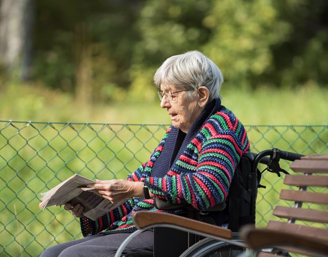 En äldre dam sitter utomhus i sin rullstol och läser tidningen