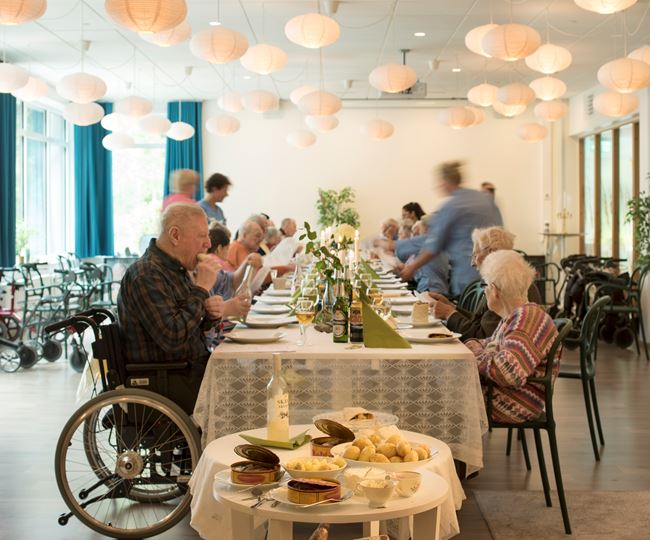Äldre personer sitter runt ett fin dukat bord och äter tillsammans