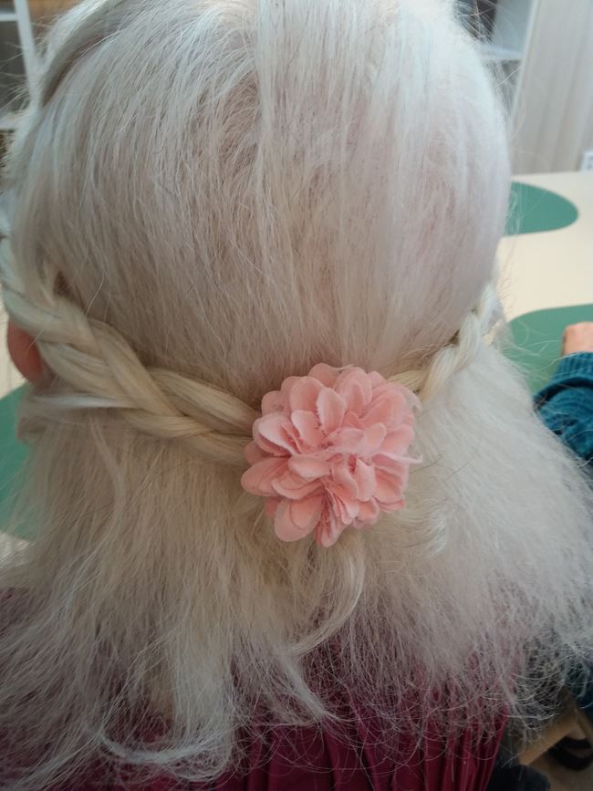 En äldre dam har en fin blomma av tyg i sitt hår