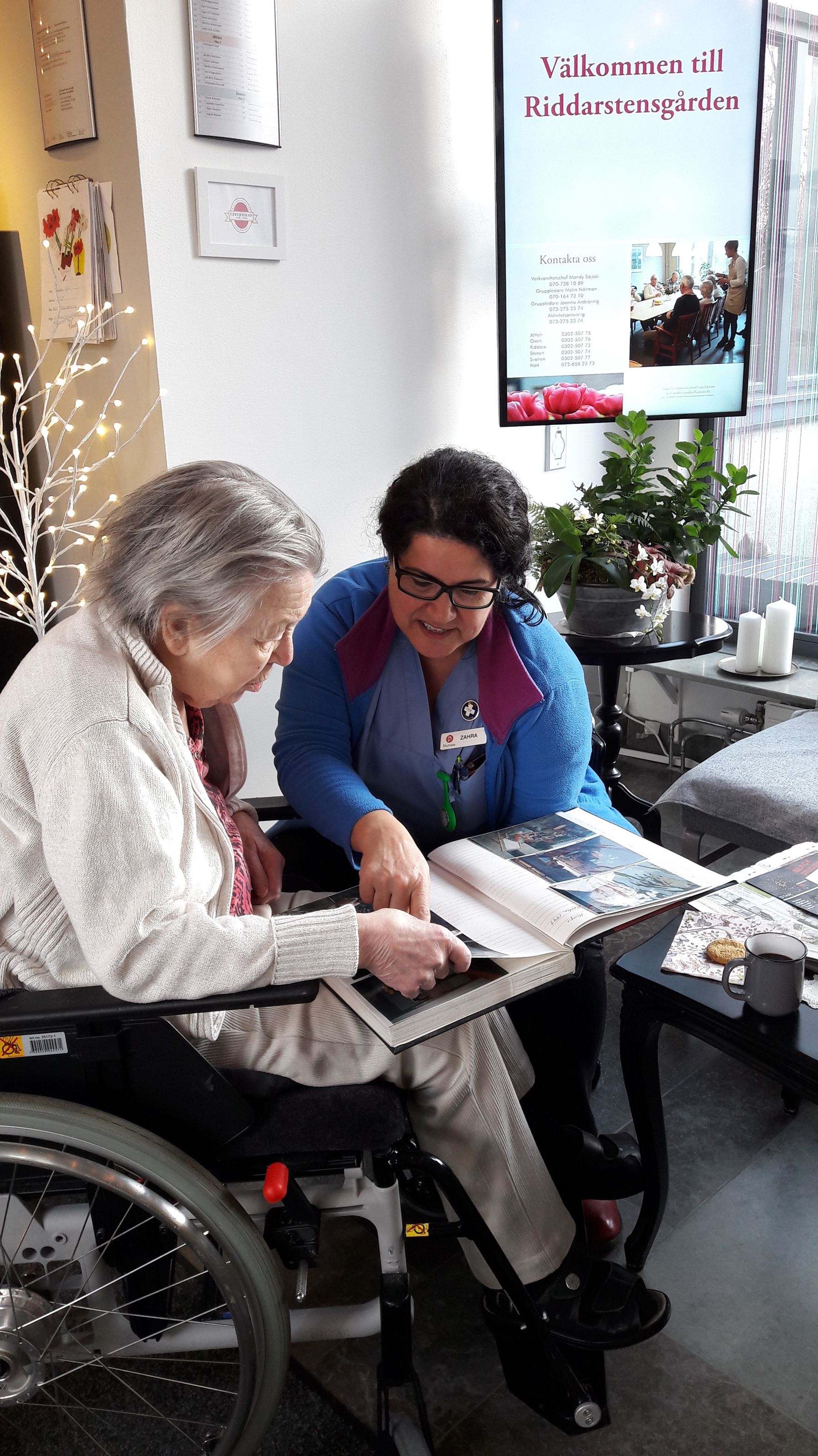 En äldre dam och personal sitter och tittar i ett fotoalbum.