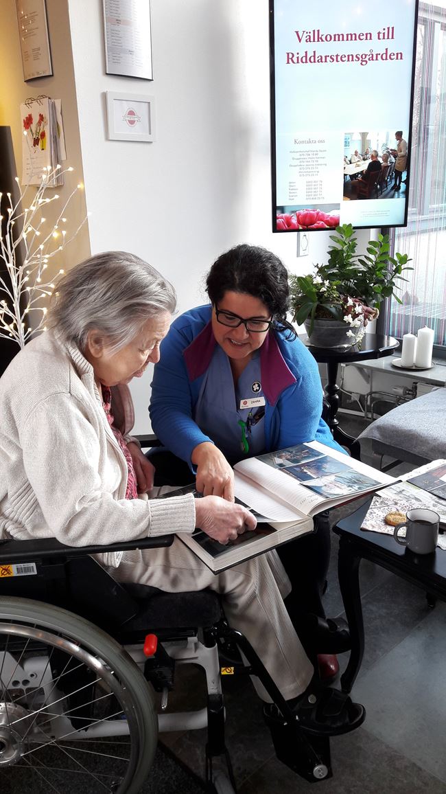En äldre dam och personal sitter och tittar i ett fotoalbum.