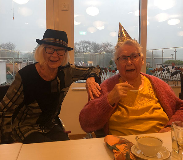 De äldre sitter i fikarummet med fina hattar på sig