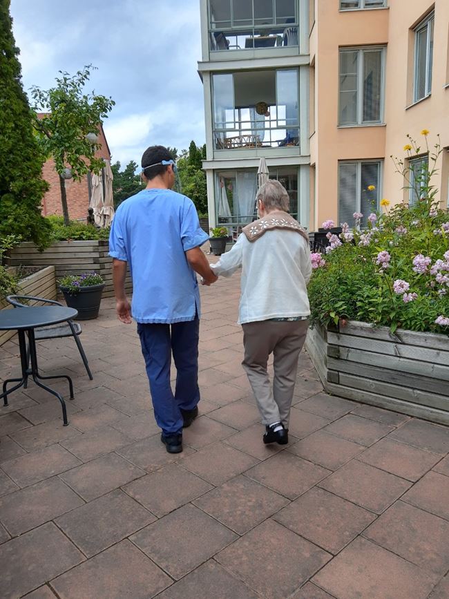En anställs och en äldre person tar en promenad ute på gården
