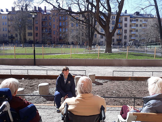 Några äldre kunder sitter i en park med en vårdare. De samtalar