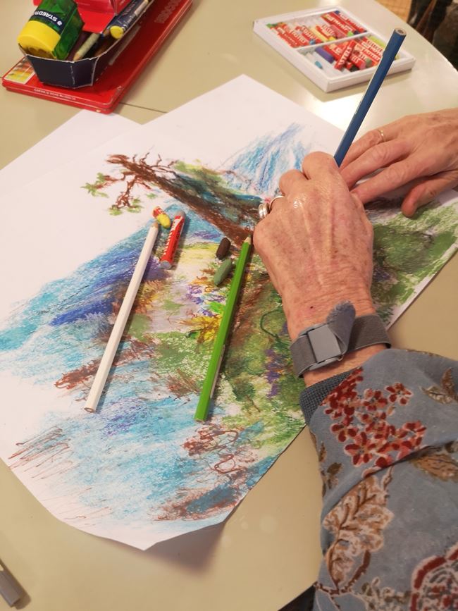 Äldre dam ritar med pennor en bild på ett träd