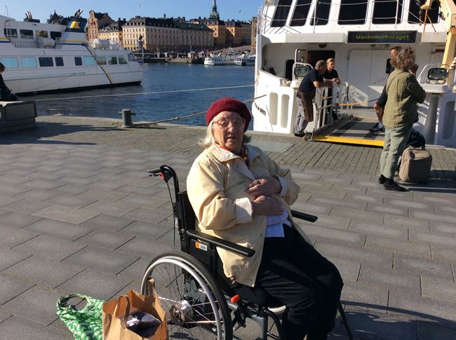 En äldre dam sitter i en rullstol på kajen vid Skärgårdsbåten.